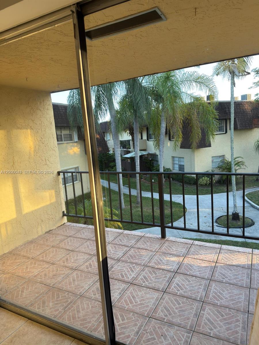 A tiled balcony overlooks a courtyard with palm trees and apartment buildings — 9108 SW 137th Ter # 3, Miami FL 33176, MIAMI, FL