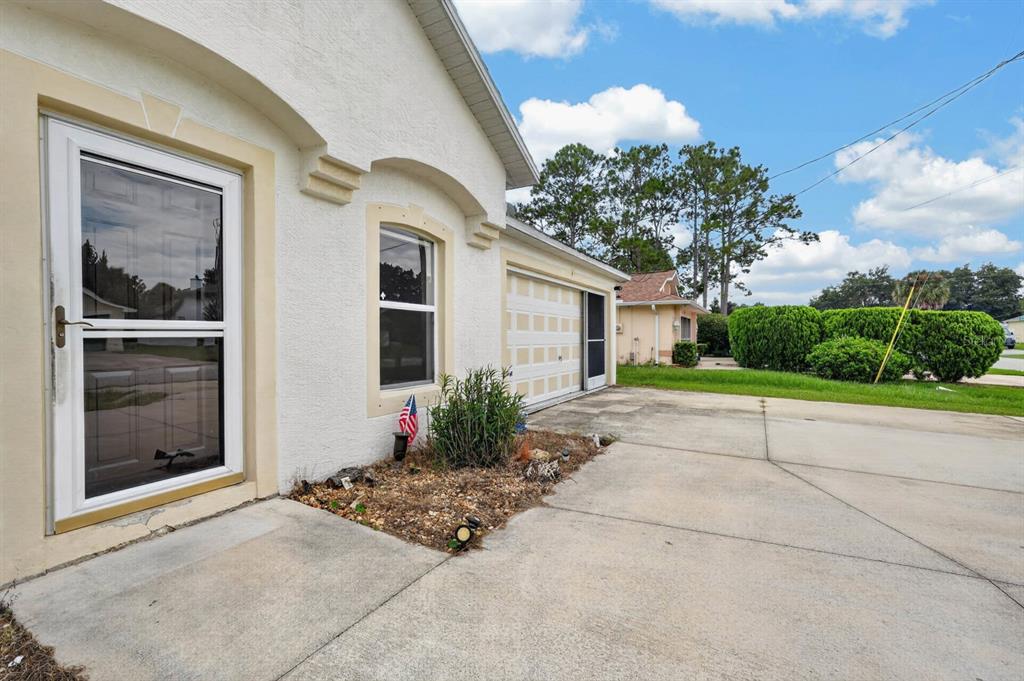 A white stucco house exterior features a front door, a window, and a garage — 6 BROWNSTONE LANE, PALM COAST, FL