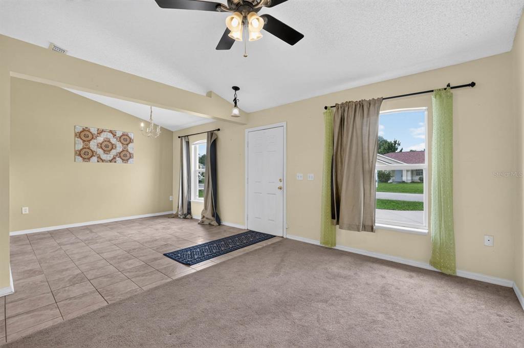 A living room with beige carpet, a tiled dining area, and a white front door — 6 BROWNSTONE LANE, PALM COAST, FL