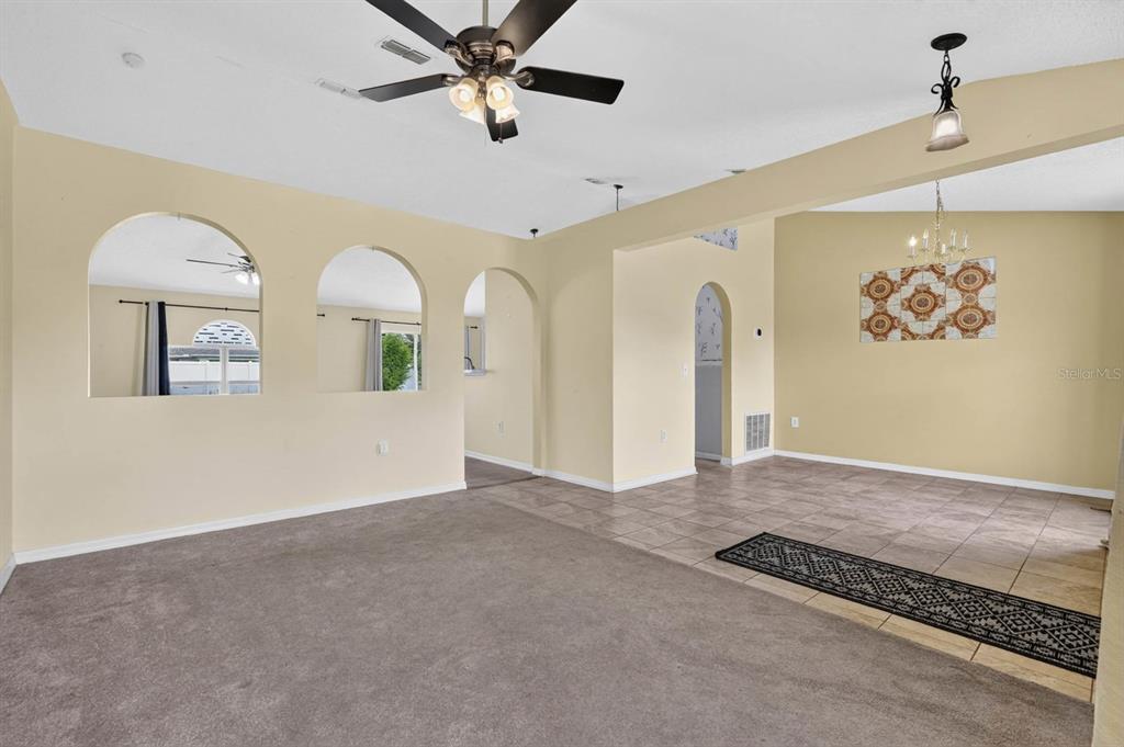 A living room with carpeted flooring, arched wall cutouts, and an adjacent tiled dining area — 6 BROWNSTONE LANE, PALM COAST, FL