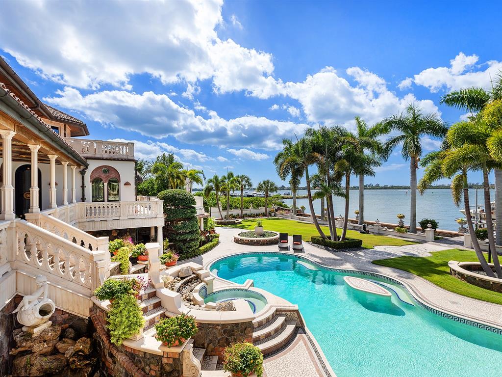 A luxury waterfront home features a tiered swimming pool, stone patio, and palm trees — 1310 S LAKE SHORE DRIVE, SARASOTA, FL