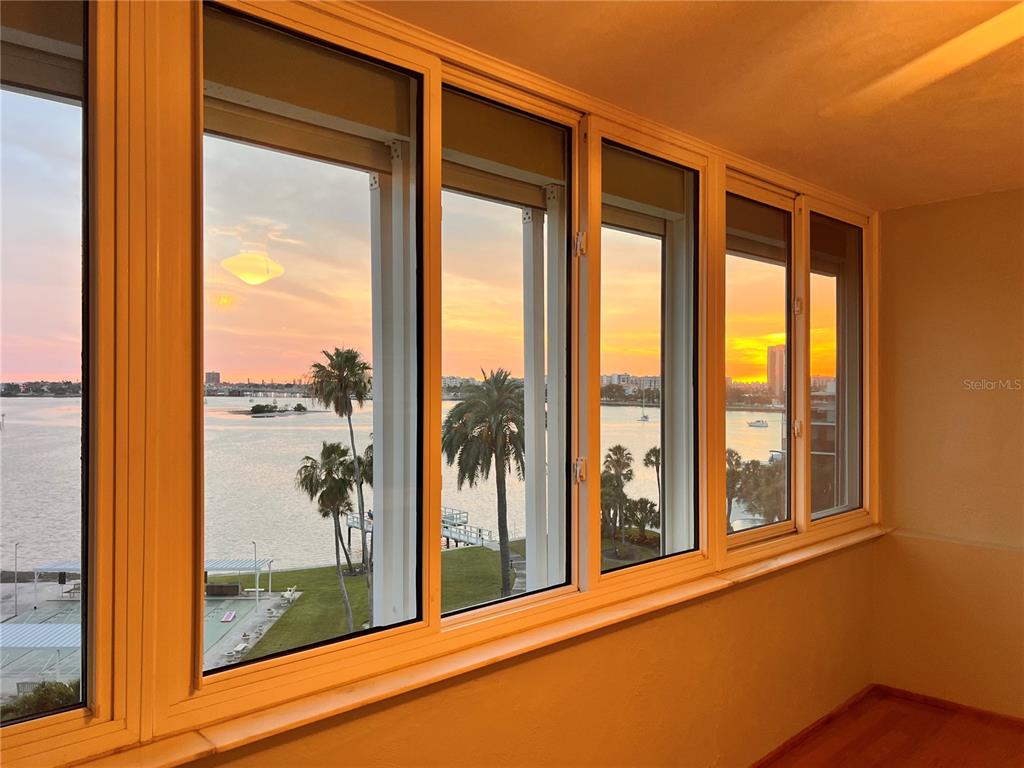 A sunroom with large windows overlooking a waterfront view at sunset — 1868 SHORE DRIVE S UNIT 607, SOUTH PASADENA, FL