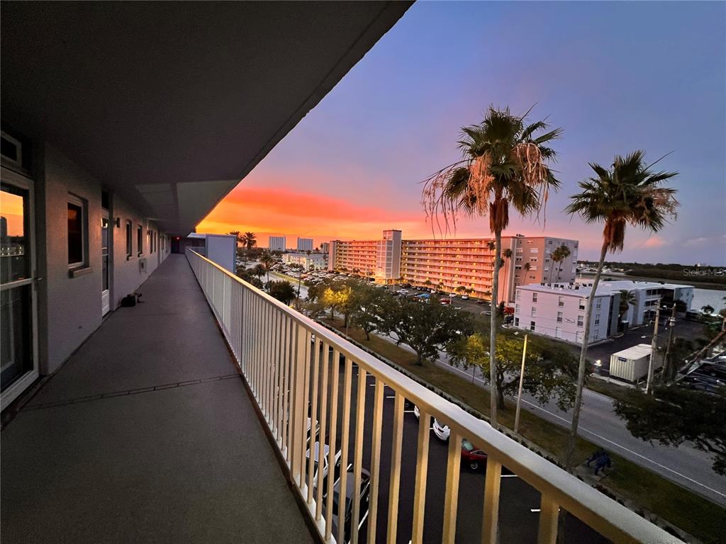 An elevated outdoor walkway overlooks a parking lot and apartment buildings during a sunset — 1868 SHORE DRIVE S UNIT 607, SOUTH PASADENA, FL