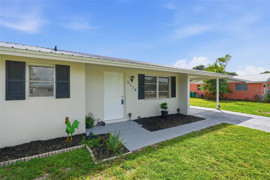 A single-story house with a white exterior, dark shutters, a metal roof, and a carport — 3178 SUNRISE TRAIL, PORT CHARLOTTE, FL