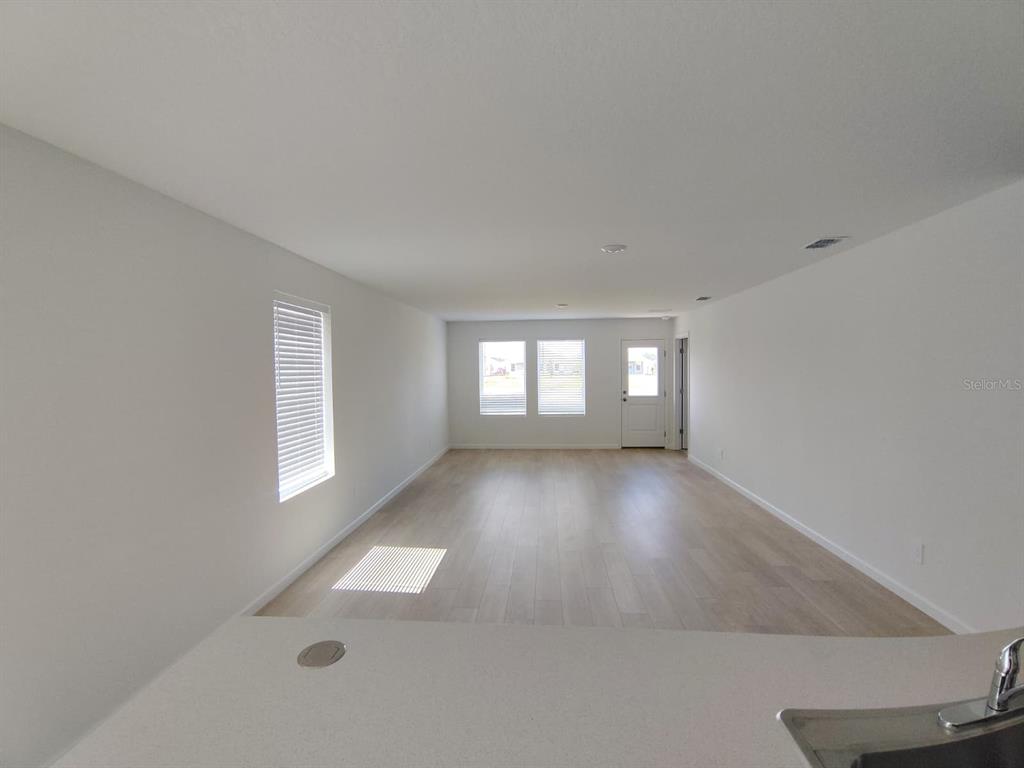 An empty living room features light-colored wood flooring, white walls, and a sliding glass door — 5542 PIMENTA COURT, KISSIMMEE, FL