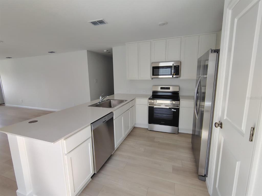 A modern kitchen features white cabinets, stainless steel appliances, and a quartz-topped island — 5542 PIMENTA COURT, KISSIMMEE, FL