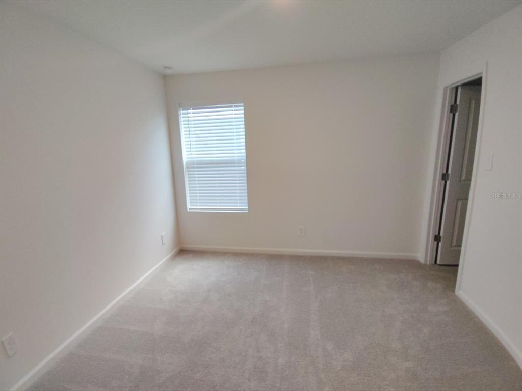 An empty bedroom features neutral walls, beige carpeting, and a single window with white blinds — 5542 PIMENTA COURT, KISSIMMEE, FL