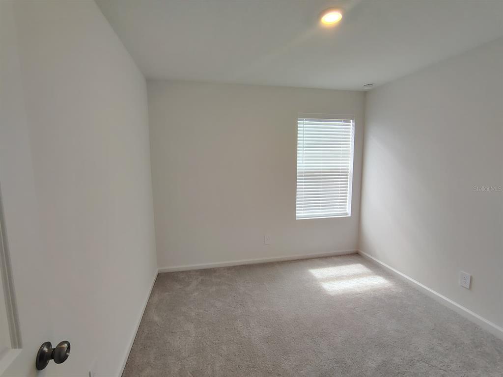 An empty bedroom features white walls, gray carpet, and a single window with blinds — 5542 PIMENTA COURT, KISSIMMEE, FL