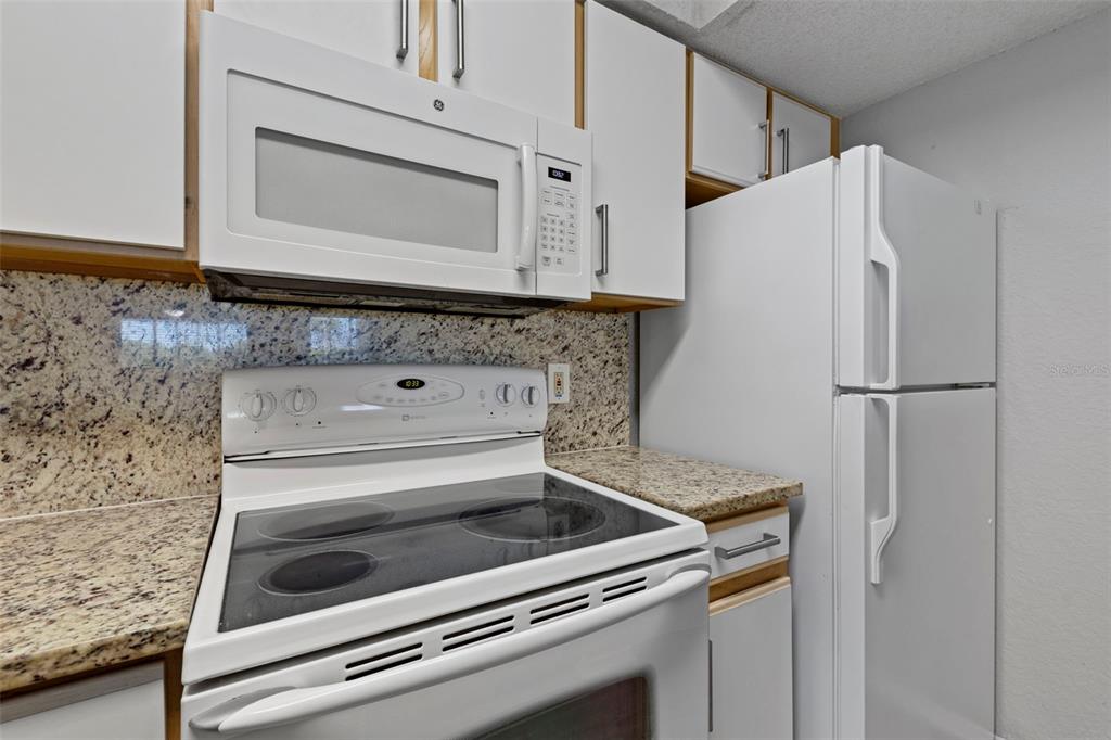A kitchen features white appliances, granite countertops, and white cabinetry — 2212 GRAND CAYMAN COURT UNIT 1616, KISSIMMEE, FL