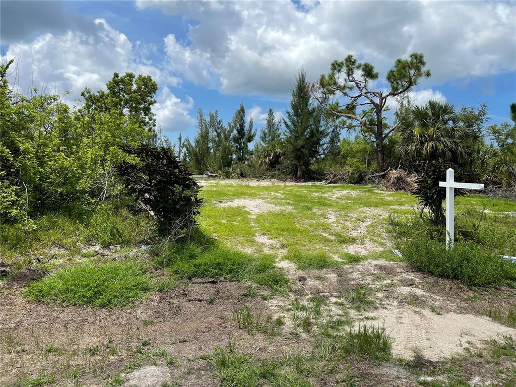 A vacant, grassy lot with sandy patches features a white sign post and surrounding trees — 15181 LYNEBURG AVENUE, PORT CHARLOTTE, FL