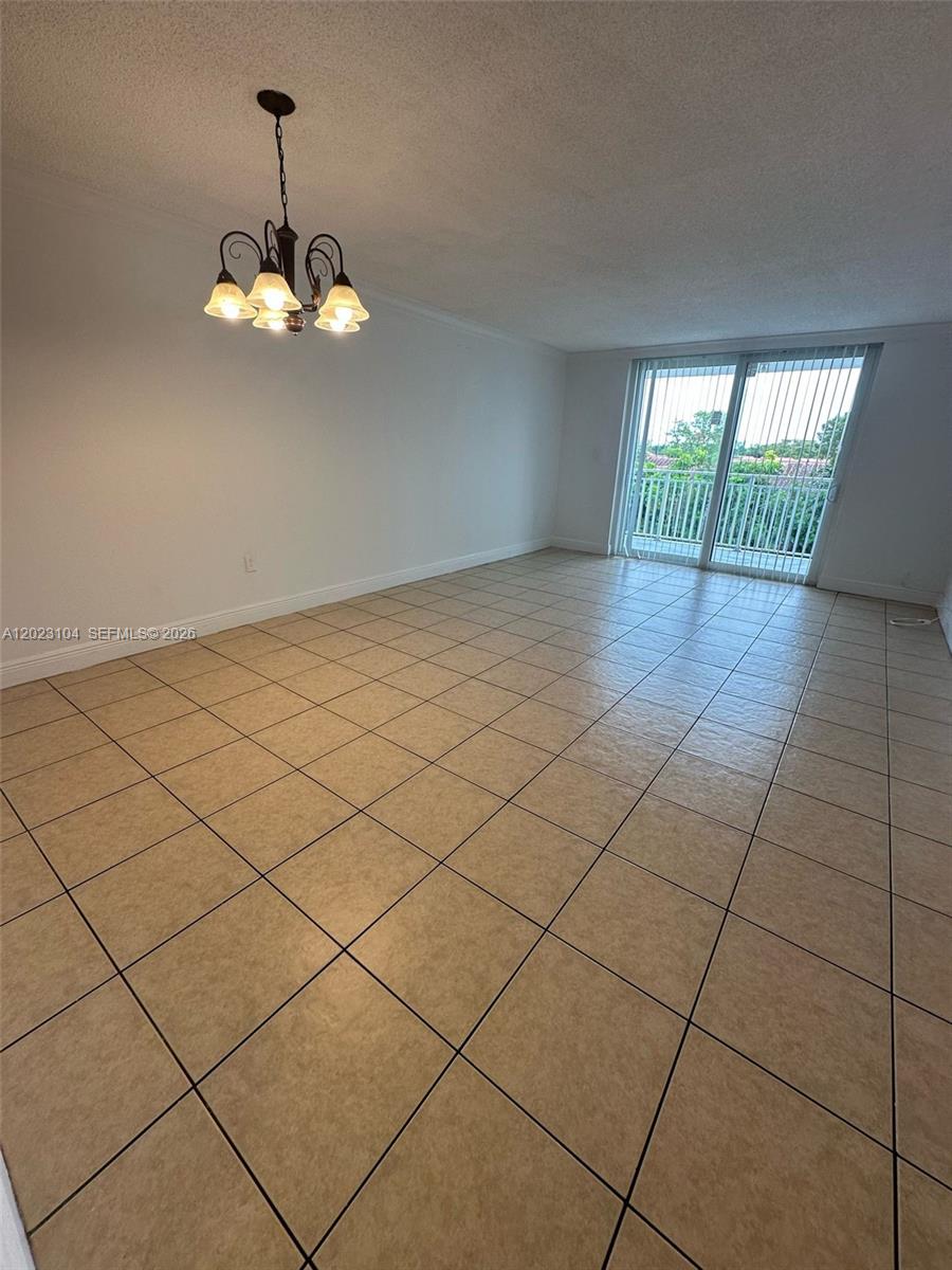 An empty room features beige tile flooring, white walls, and a hanging chandelier — 6930 Miami Gardens Dr # 408, Hialeah FL 33015, HIALEAH, FL