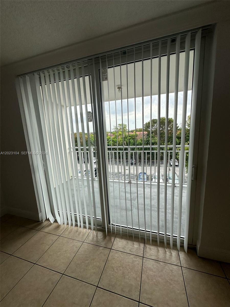 A room with beige tile flooring features a large sliding glass door with vertical blinds — 6930 Miami Gardens Dr # 408, Hialeah FL 33015, HIALEAH, FL