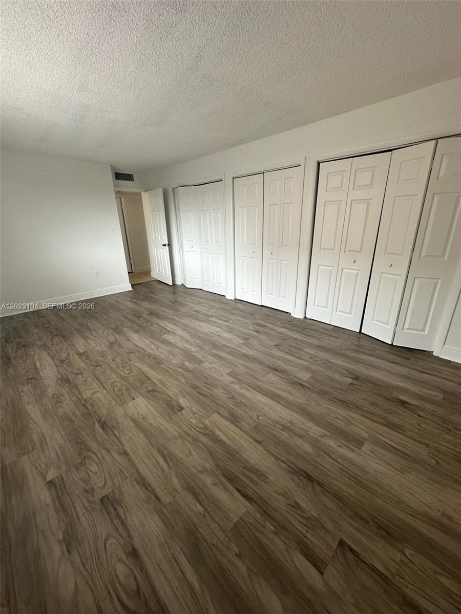 An empty room features wood-look flooring, white walls, and multiple sets of white closet doors — 6930 Miami Gardens Dr # 408, Hialeah FL 33015, HIALEAH, FL
