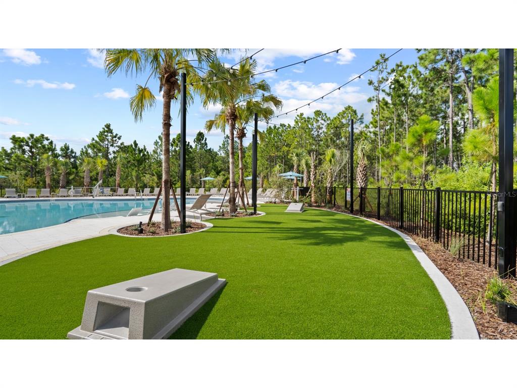 A swimming pool area features a green lawn with cornhole boards and string lights — 22 GARNI DRIVE, PALM COAST, FL