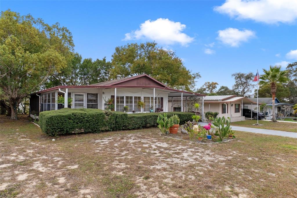 A single-story manufactured home with a covered porch, large hedge, and sandy front yard — 12118 FAIRWAY AVENUE, BROOKSVILLE, FL