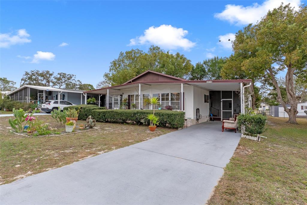 A single-story manufactured home with a concrete driveway, carport, and landscaped front yard — 12118 FAIRWAY AVENUE, BROOKSVILLE, FL