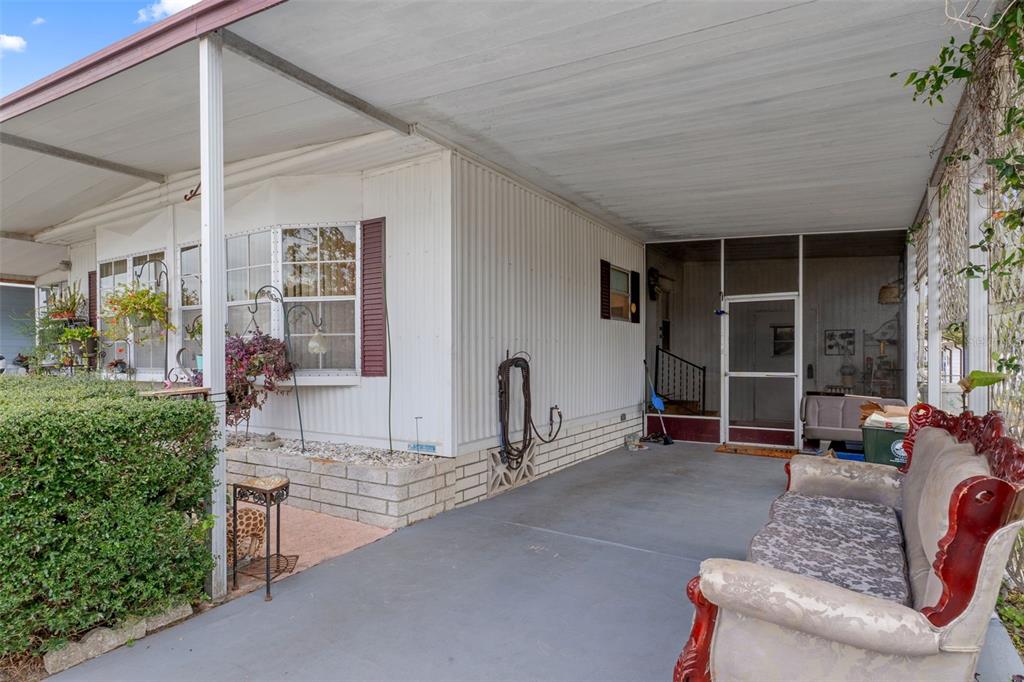A covered concrete carport sits beside a mobile home with a screened-in porch entrance — 12118 FAIRWAY AVENUE, BROOKSVILLE, FL