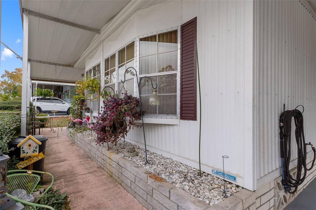 A white mobile home exterior features a covered walkway, a brick planter, and hanging plants — 12118 FAIRWAY AVENUE, BROOKSVILLE, FL