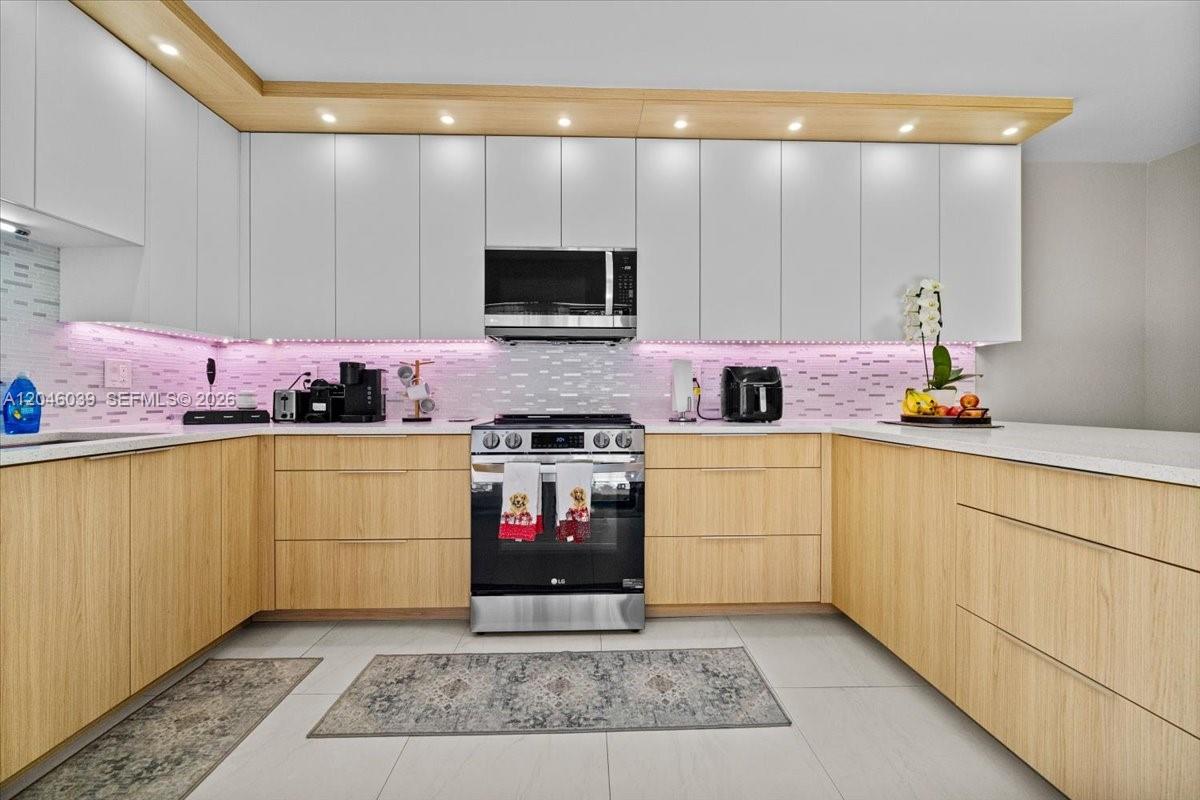 A modern kitchen features light wood lower cabinets, white upper cabinets, and pink under-cabinet lighting — 2891 SW 11th Pl, Deerfield Beach FL 33442, DEERFIELD BEACH, FL