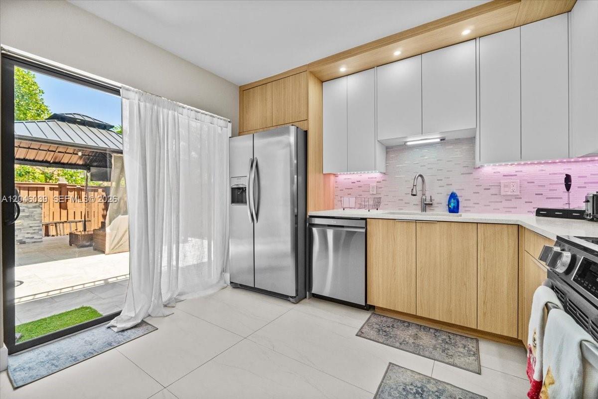 A modern kitchen features light wood cabinets, white upper cabinets, stainless steel appliances, and tile flooring — 2891 SW 11th Pl, Deerfield Beach FL 33442, DEERFIELD BEACH, FL
