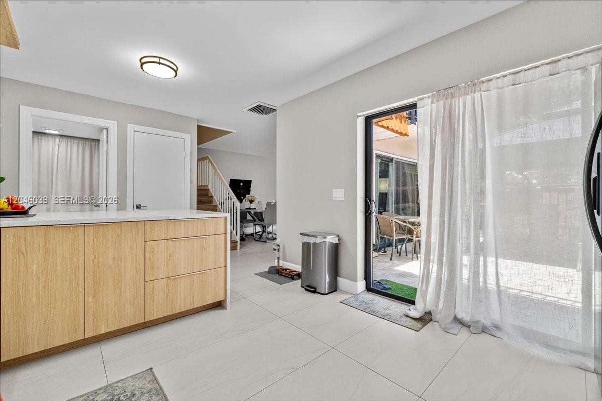 A modern kitchen features light wood cabinets, white countertops, and a sliding glass door — 2891 SW 11th Pl, Deerfield Beach FL 33442, DEERFIELD BEACH, FL