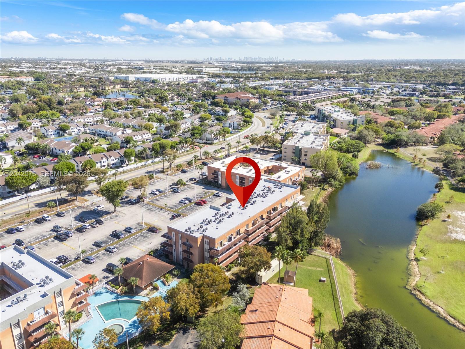 An aerial view shows a multi-story apartment building with a pool and a nearby lake — 17530 NW 68th Ave # C2003, Hialeah FL 33015, HIALEAH, FL