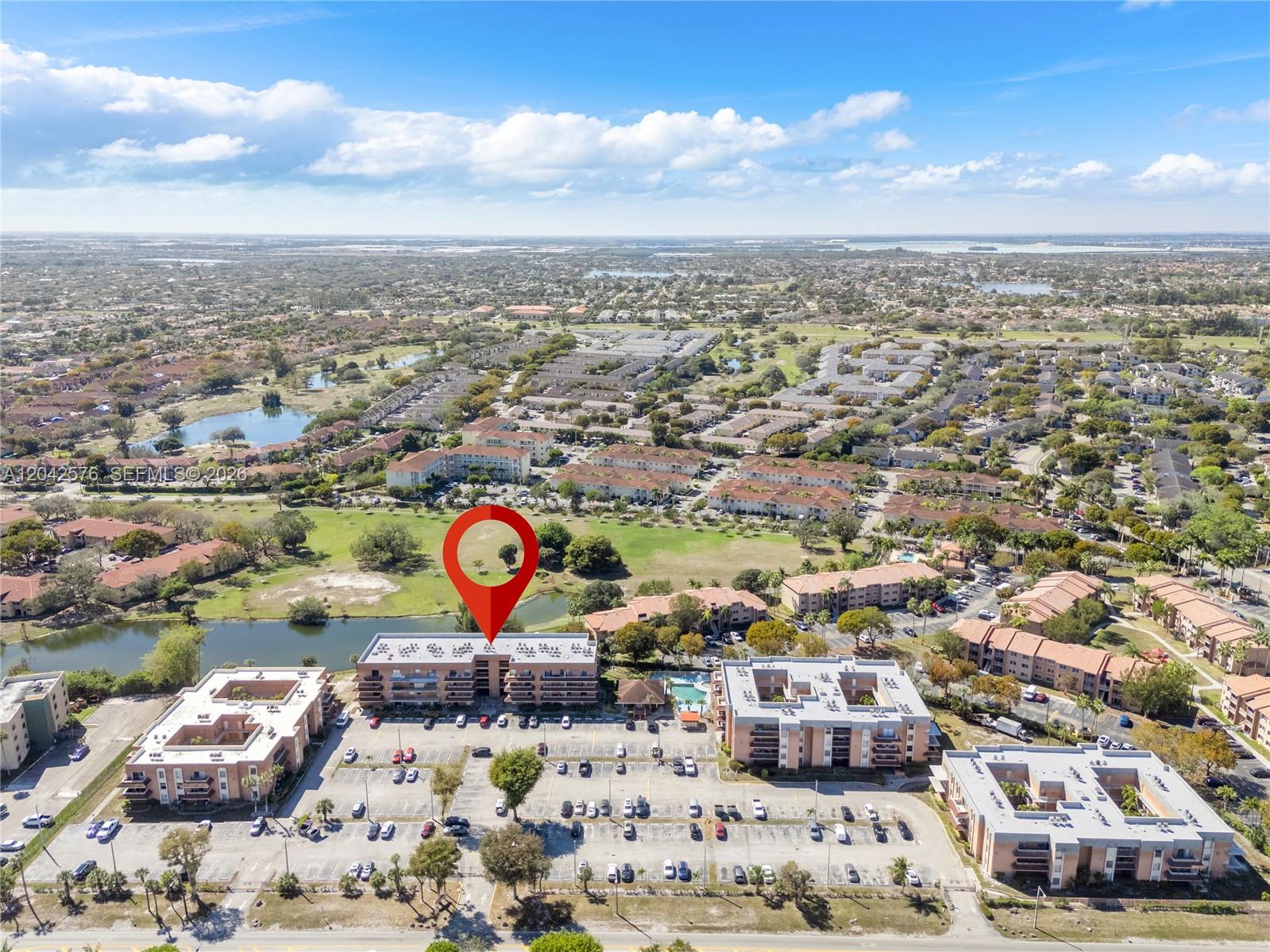 An aerial view shows a multi-story apartment complex with a parking lot and pond — 17530 NW 68th Ave # C2003, Hialeah FL 33015, HIALEAH, FL