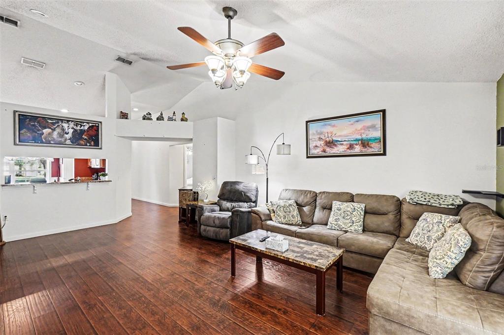 A living room features a vaulted ceiling, a ceiling fan, wood flooring, and a sectional sofa — 531 HEATHER GLEN DRIVE, WINTER HAVEN, FL