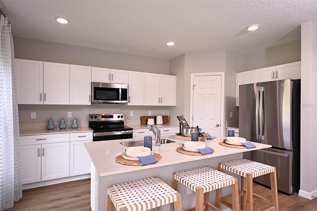 A modern kitchen features white cabinetry, stainless steel appliances, a quartz island, and woven barstools — 1760 VANILLA STREET, LAKE HAMILTON, FL