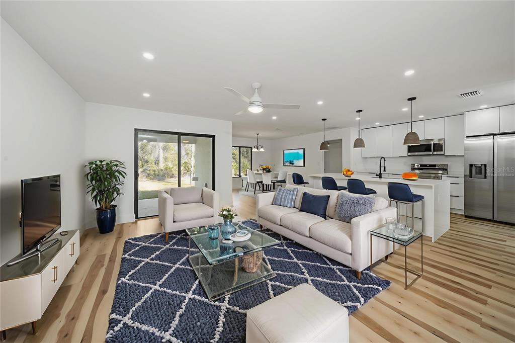 A modern open-concept living room and kitchen featuring light wood floors and a blue rug — 15460 CHAMBERLAIN BOULEVARD, PORT CHARLOTTE, FL