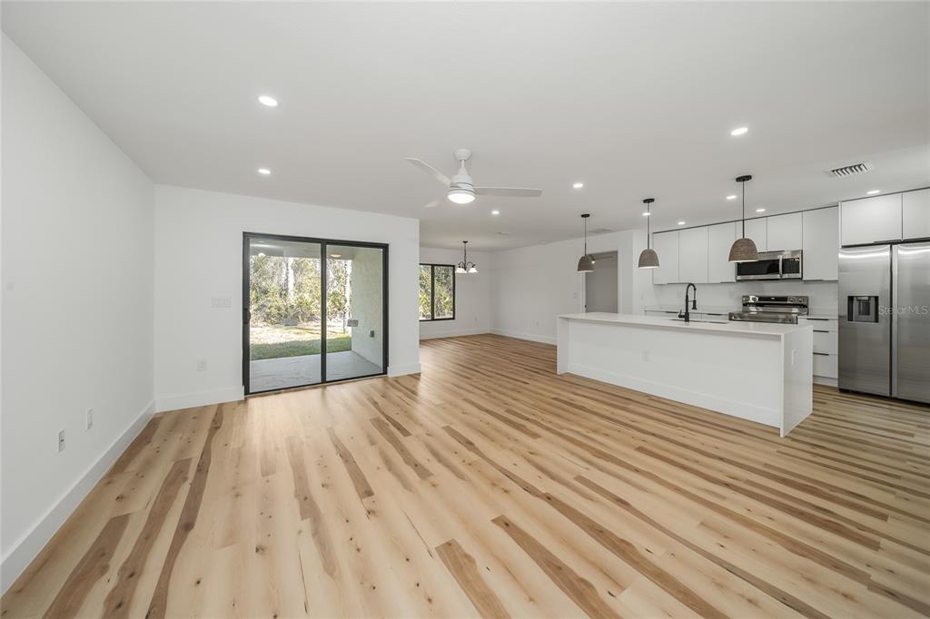 An open-concept kitchen and living area features light wood flooring, white cabinetry, and sliding doors — 15460 CHAMBERLAIN BOULEVARD, PORT CHARLOTTE, FL