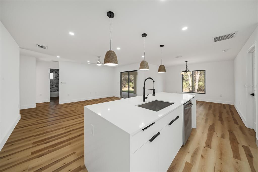 A modern kitchen island with a sink sits in an open-concept room with wood floors — 15460 CHAMBERLAIN BOULEVARD, PORT CHARLOTTE, FL