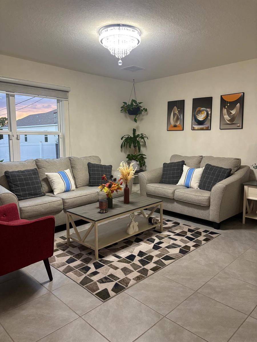 A living room features two gray sofas, a geometric rug, and a crystal chandelier — 1598 Leeward Avenue SE, Palm Bay FL 32909, PALM BAY, FL