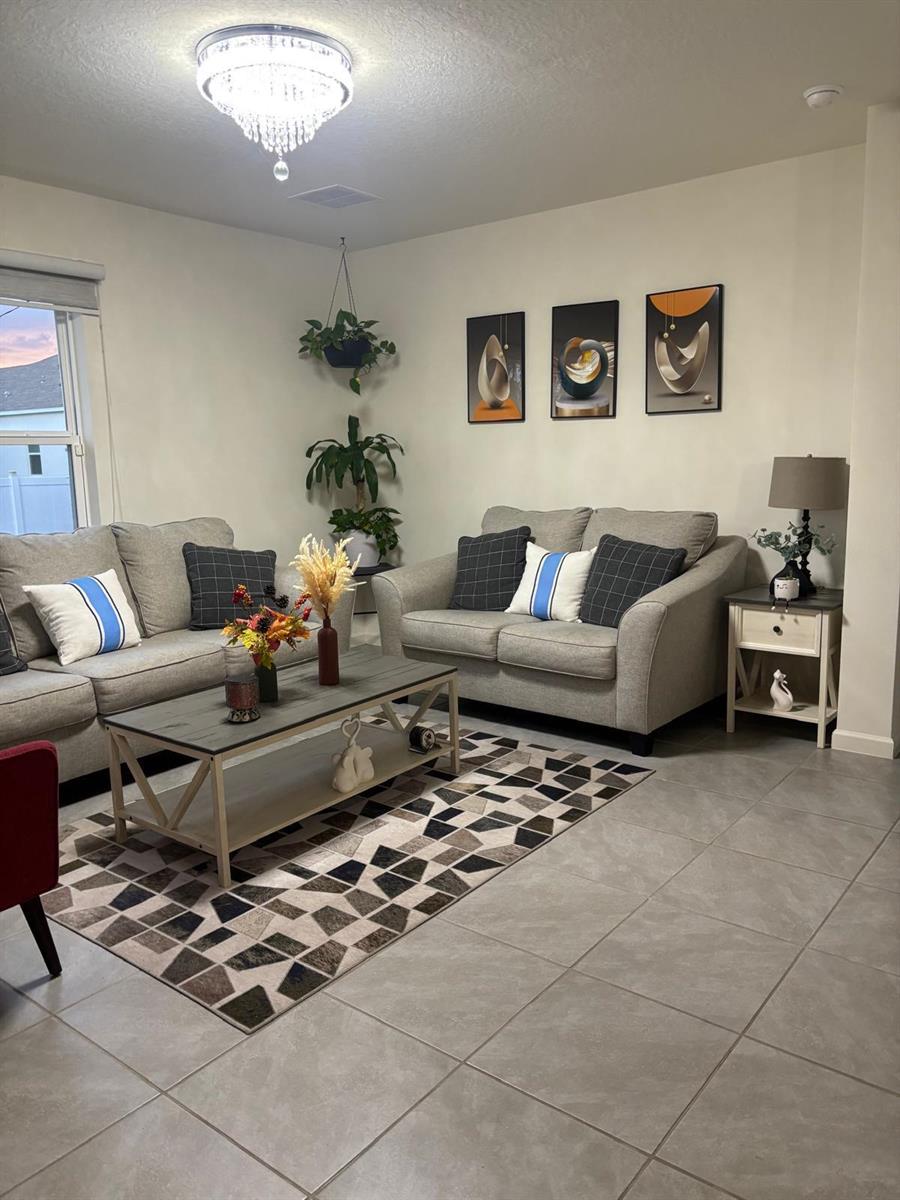 A living room features gray sofas, a geometric rug, a coffee table, and wall art — 1598 Leeward Avenue SE, Palm Bay FL 32909, PALM BAY, FL