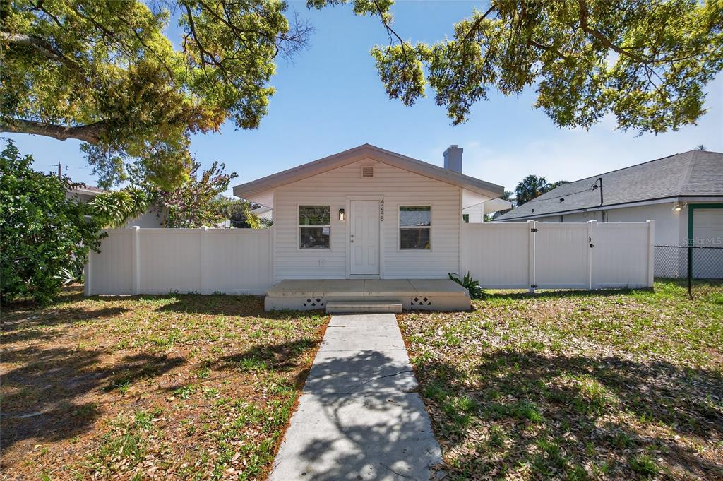 A small, single-story house with white siding stands behind a white vinyl privacy fence — 4248 4TH AVENUE S, ST PETERSBURG, FL