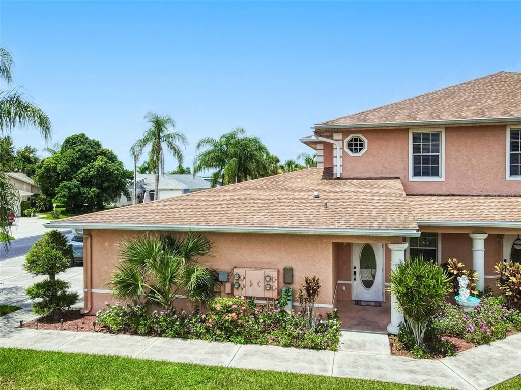 A tan two-story house with a shingled roof, a front porch, and landscaped garden beds — 19977 LAKE VISTA CIRCLE UNIT 17D, LEHIGH ACRES, FL