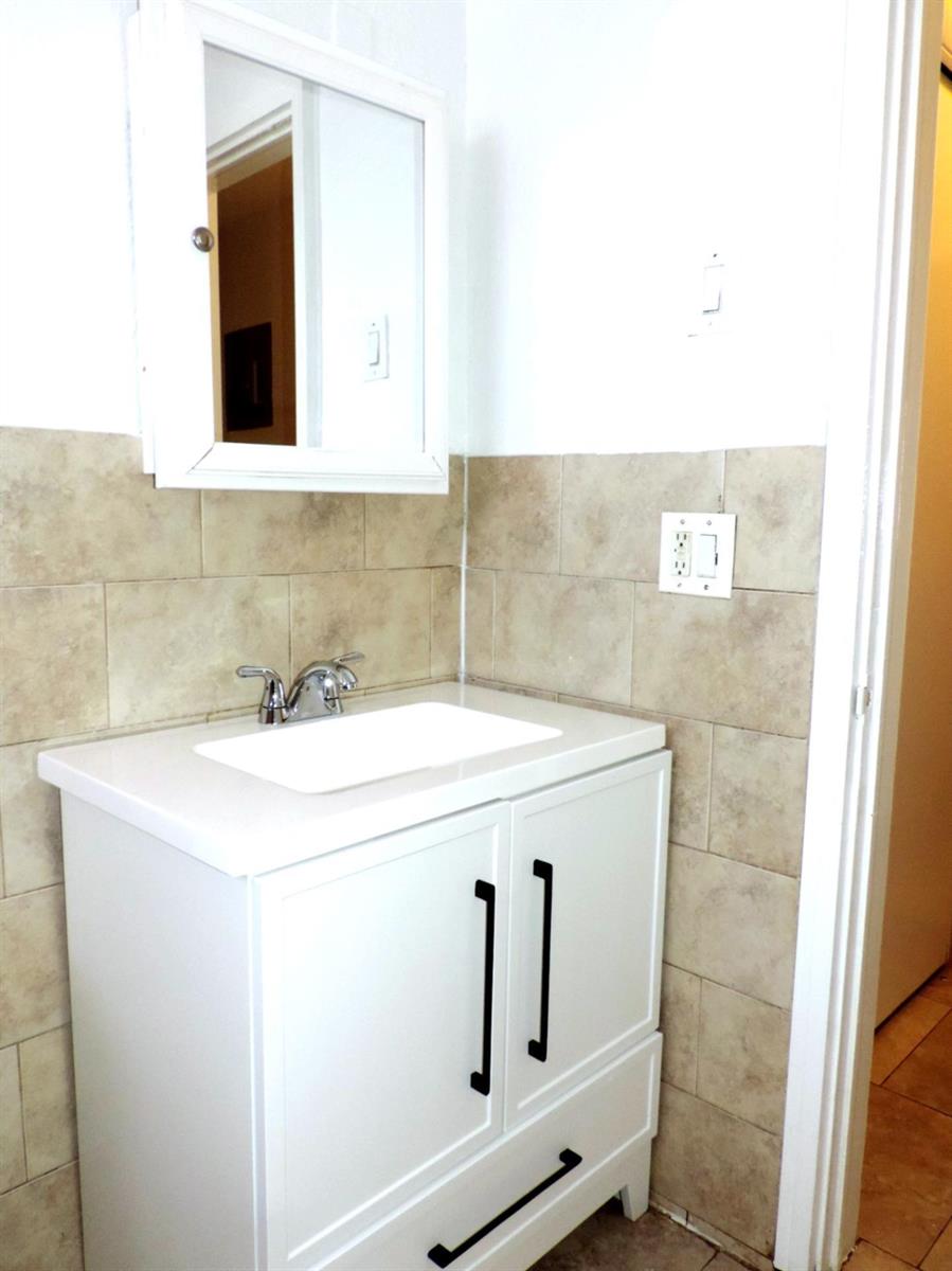 A bathroom vanity with a white cabinet, rectangular sink, and beige tiled walls — 1621 SW 6th Avenue # 2, Pompano Beach FL 33060, POMPANO BEACH, FL