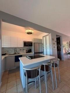 A kitchen features a white island with bar stools, stainless steel appliances, and white cabinetry — 1 HARBOUR LAKES UNIT 53, HUMACAO, PR