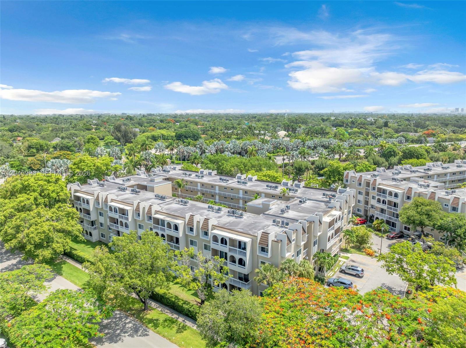 An aerial view shows a multi-story apartment complex surrounded by lush green trees and landscaping — 8101 Camino Real # 402, Miami FL 33143, MIAMI, FL