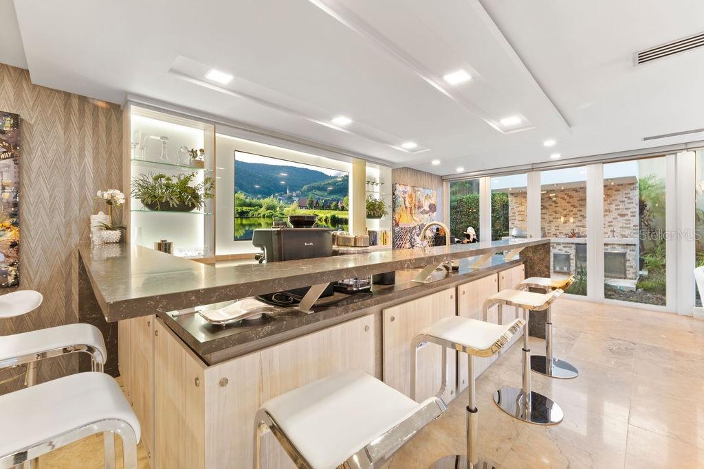A modern home bar features a stone countertop, light wood cabinetry, and glass-paneled doors — 386 DORADO BEACH EAST, DORADO, PR