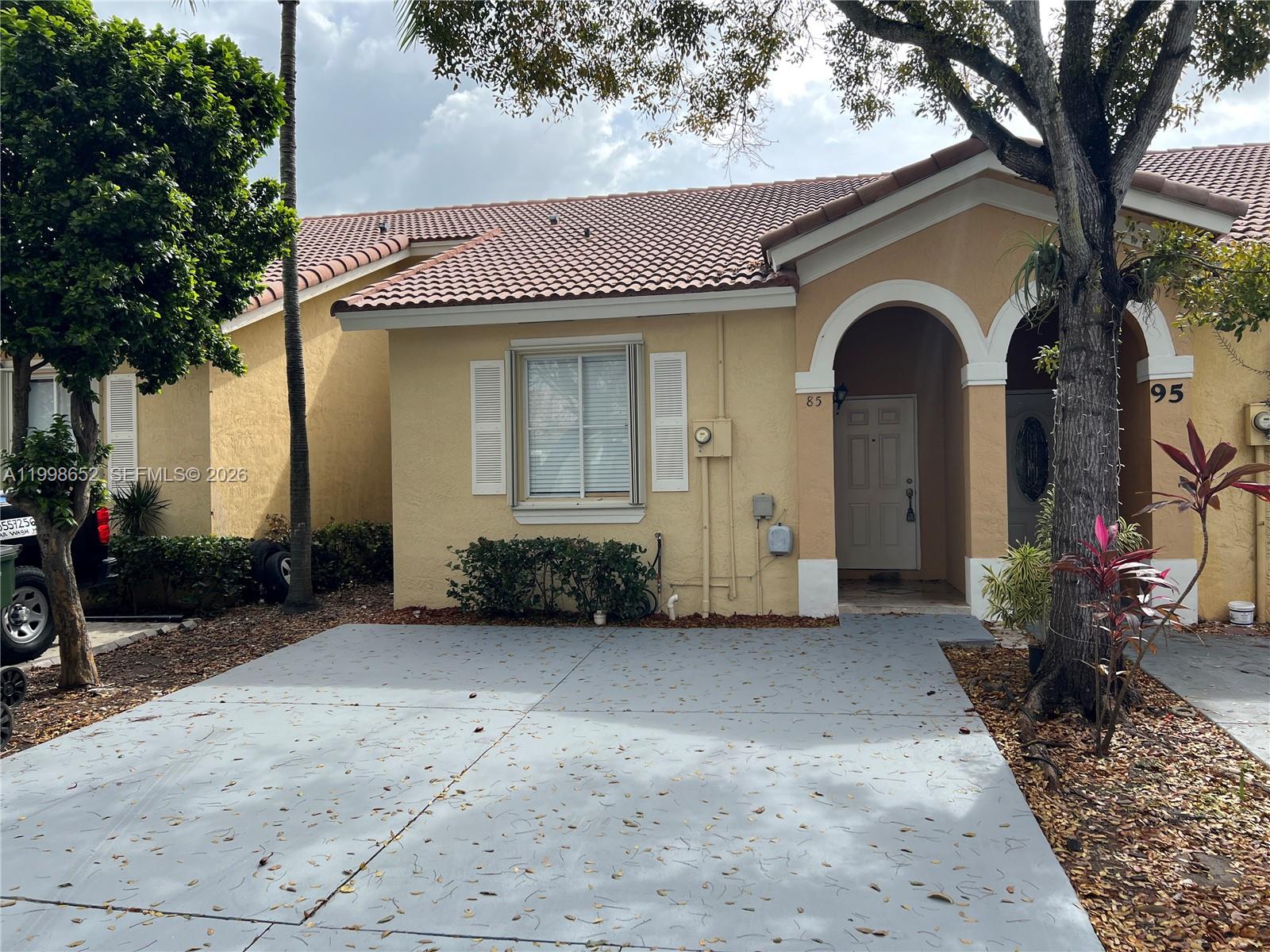 A tan stucco house features a gray concrete driveway, arched entryways, and a tiled roof — 85 SW 16 AV, Homestead FL 33030, HOMESTEAD, FL