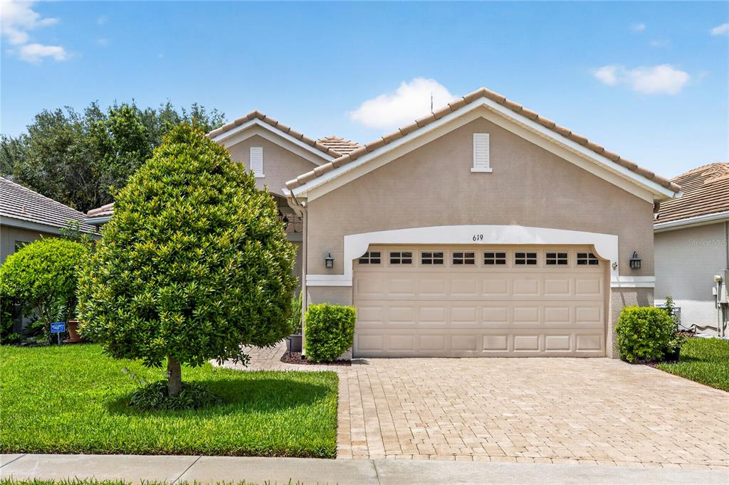 A tan single-story house features a two-car garage, a paved driveway, and a manicured lawn — 619 NEWHALL LANE, DEBARY, FL