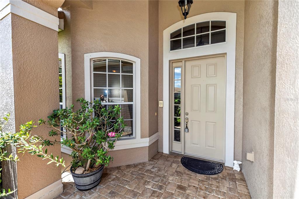A beige front door with a side window and arched transom sits on a paved porch — 619 NEWHALL LANE, DEBARY, FL