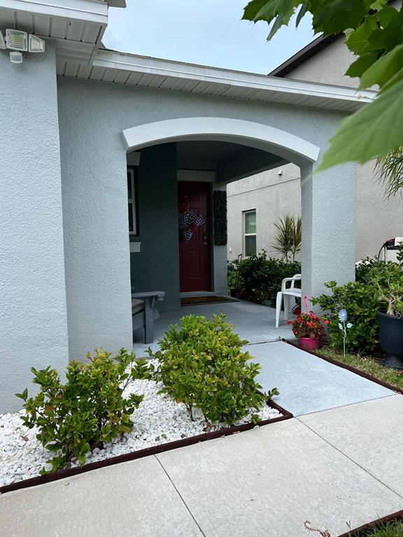 A light-colored house exterior features a covered entryway with a red door and landscaping — 7111 AMELIA COVE COURT, SUN CITY CENTER, FL