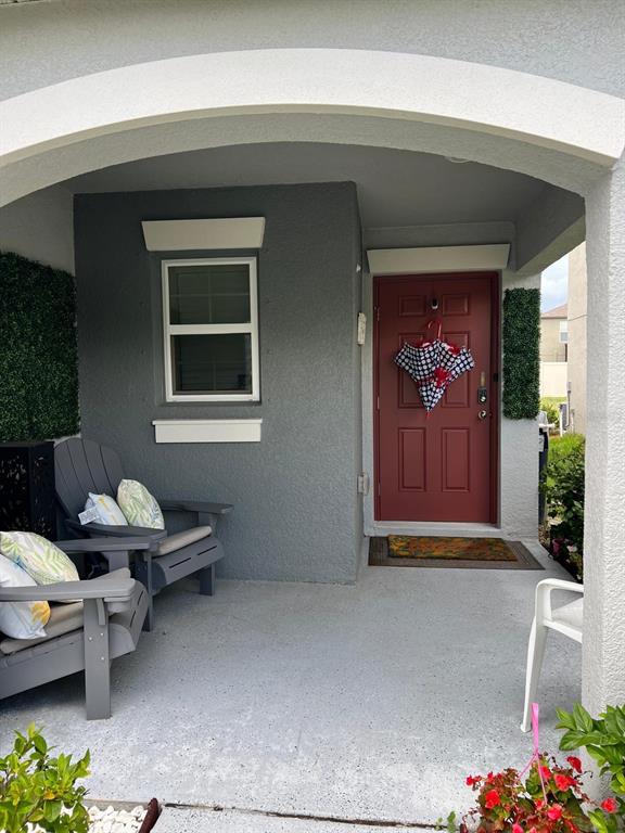 A covered front porch features gray chairs, a red front door, and decorative greenery — 7111 AMELIA COVE COURT, SUN CITY CENTER, FL