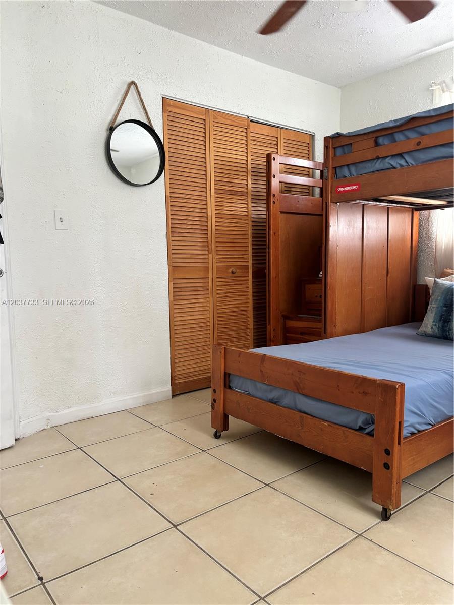 A bedroom features a wooden bunk bed, louvered closet doors, and light-colored floor tiles — DAVIE, FL