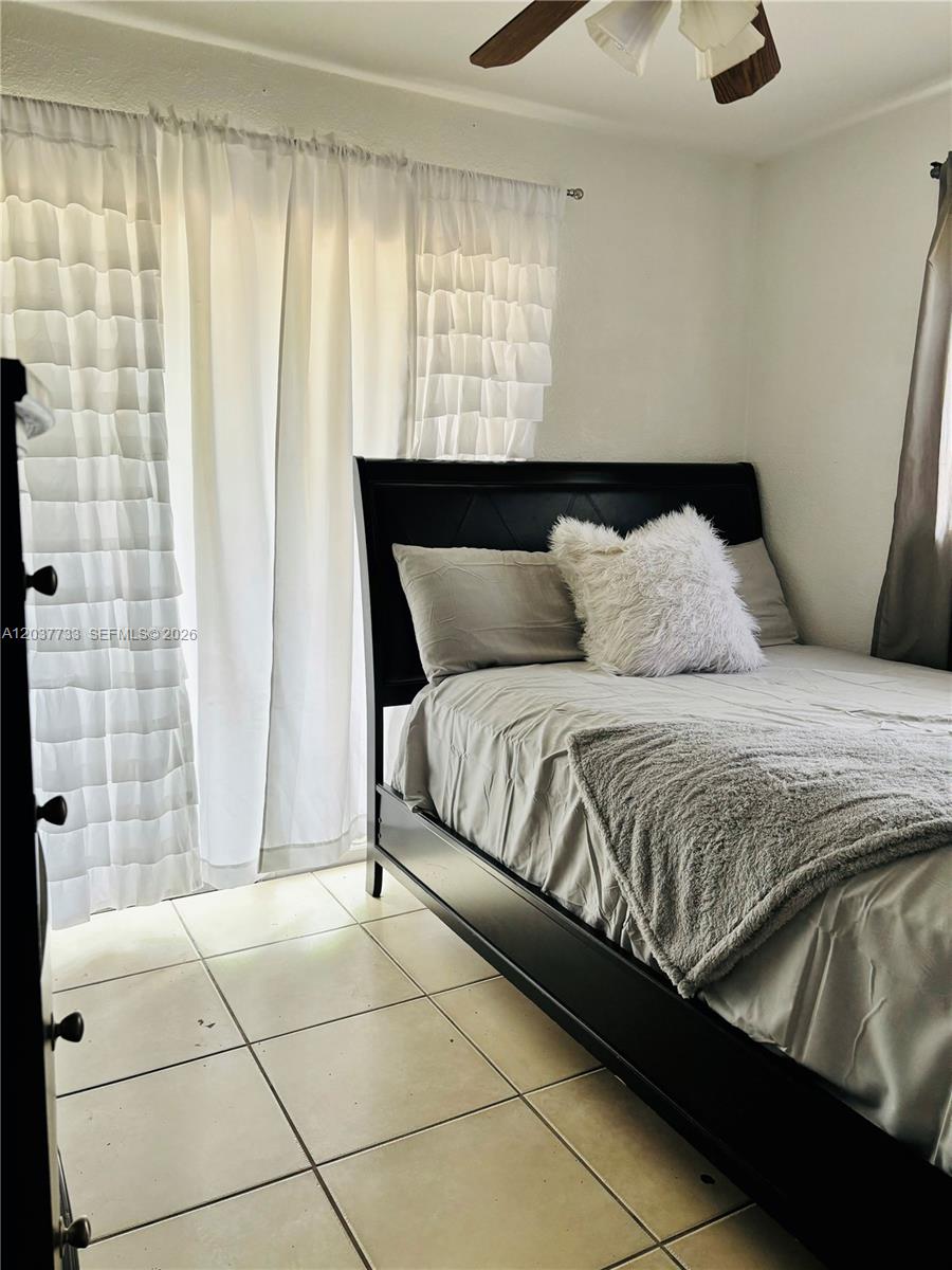 A bedroom features a black bed frame, light gray bedding, and white ruffled curtains — DAVIE, FL