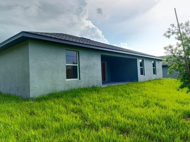 The exterior of a light-colored stucco house features a covered patio and a grassy yard — 22376 BLANCHARD AVENUE, PORT CHARLOTTE, FL
