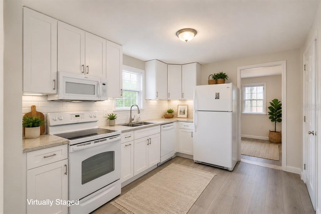 A kitchen with white cabinets, white appliances, light countertops, and light wood-look flooring — 702 W HILLSBORO STREET, PLANT CITY, FL