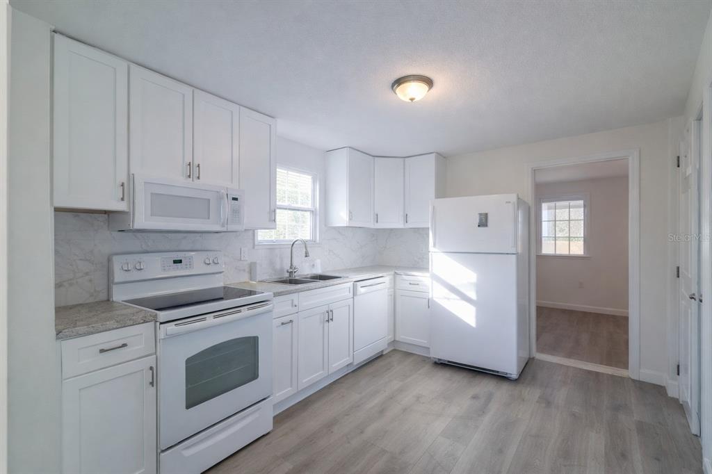 A bright kitchen features white cabinets, white appliances, marble-look backsplash, and light wood-look flooring — 702 W HILLSBORO STREET, PLANT CITY, FL